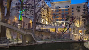 A riverside walkway with a bridge, buildings, and a reflection in the water.