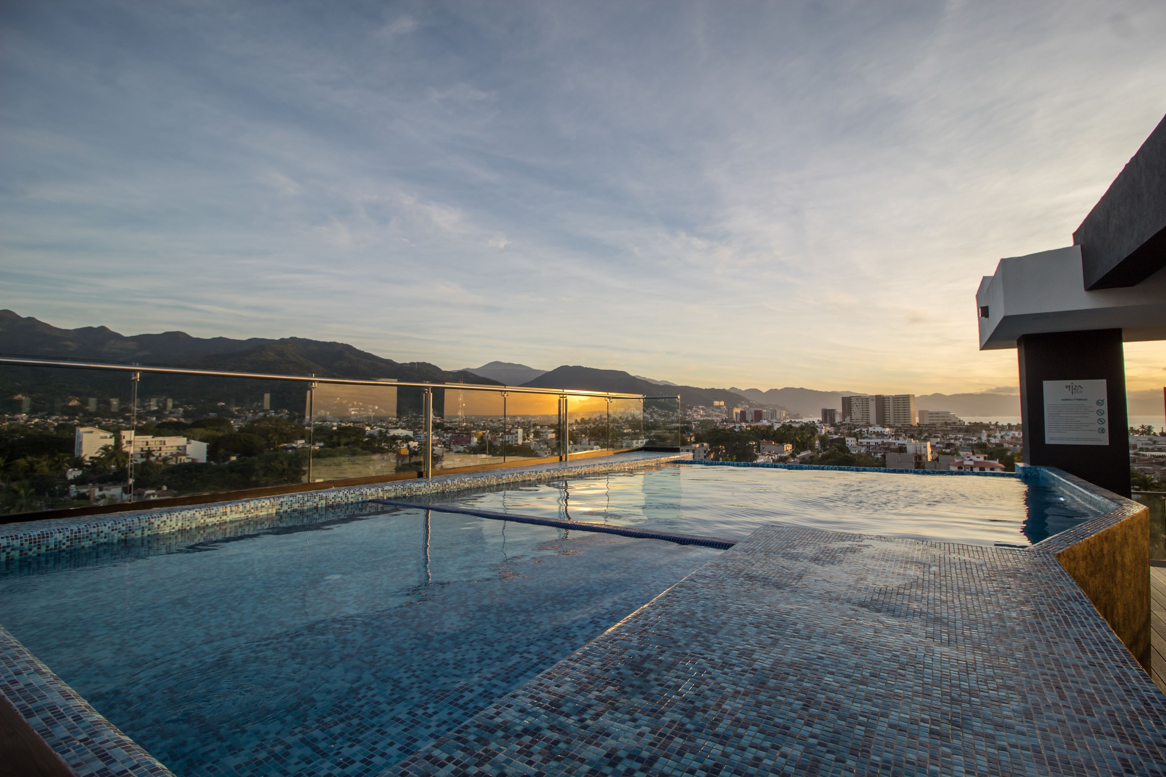 Une piscine à débordement située sur le toit, offrant une vue panoramique sur la ville, avec des montagnes et des bâtiments visibles au loin.