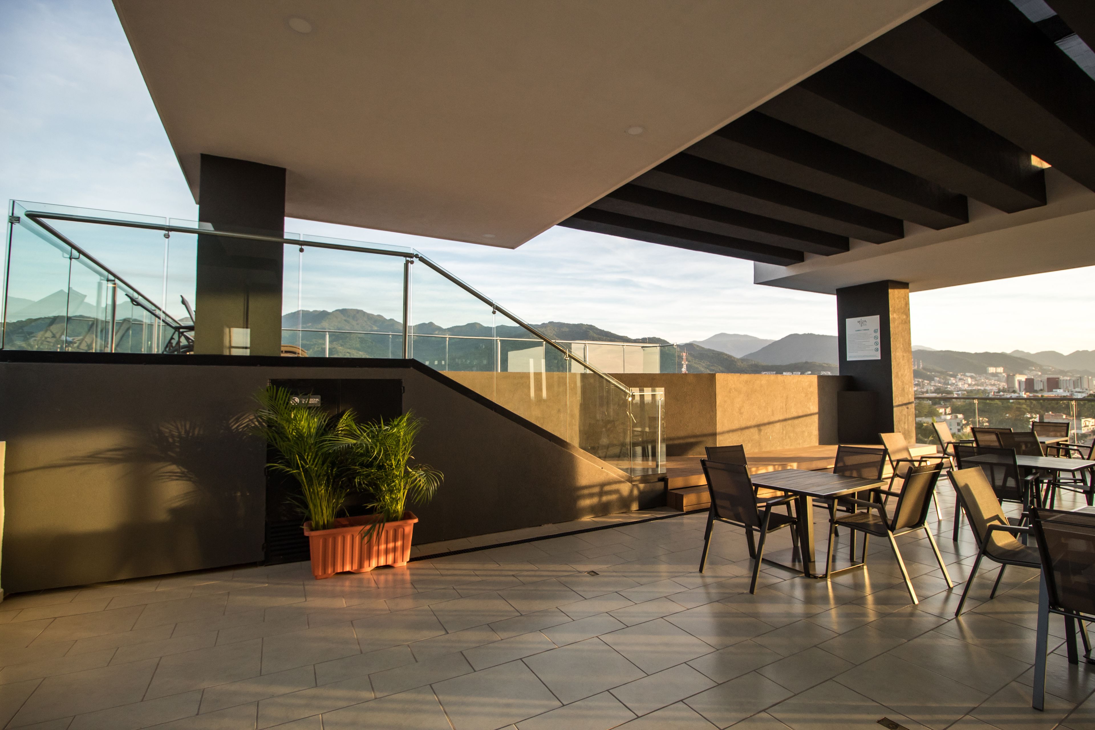 A rooftop terrace with outdoor seating, a staircase, and a view of the city and mountains.