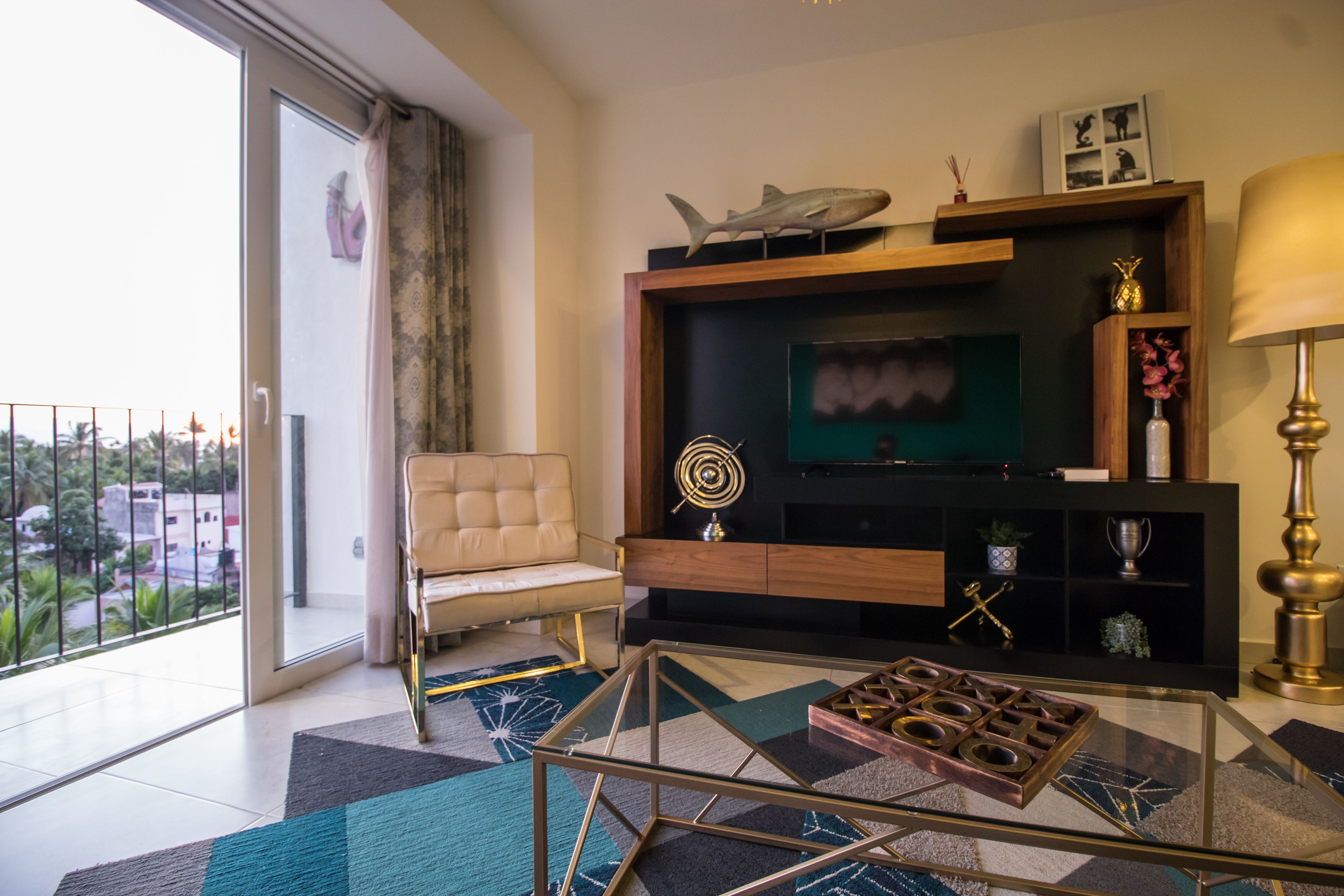 A modern living room with a glass coffee table, a sofa, a TV, and a balcony with a view.