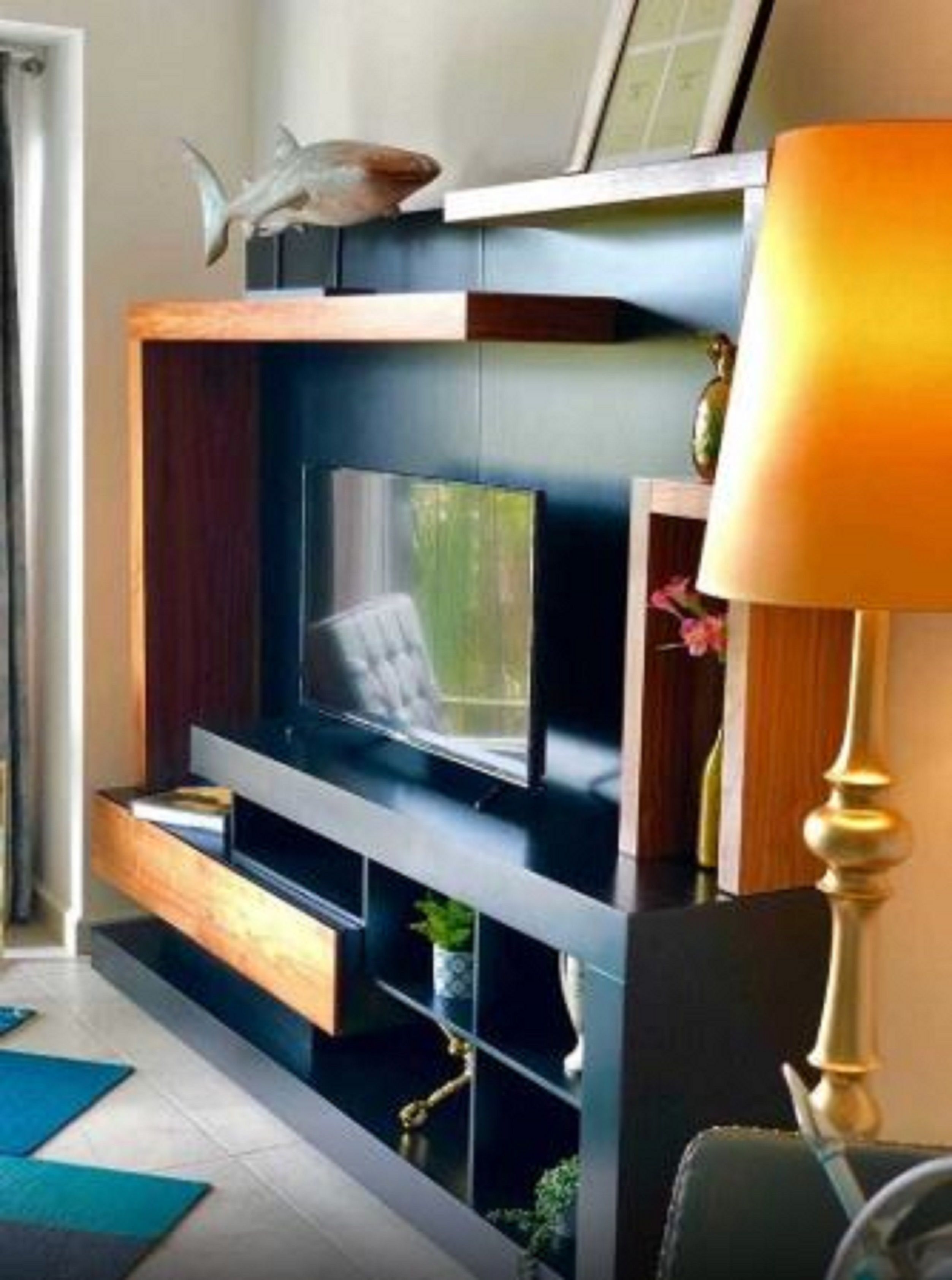 A modern living room with a flat-screen TV, wooden shelves, and a decorative fish sculpture.