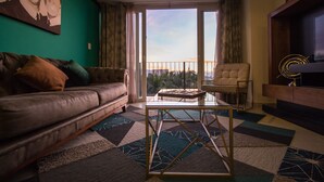 A living room with a sofa, a coffee table, and a chair. There is a large window with a view of the outdoors. - Niza Five Luxury Beach Apartments (Puerto Vallarta)
