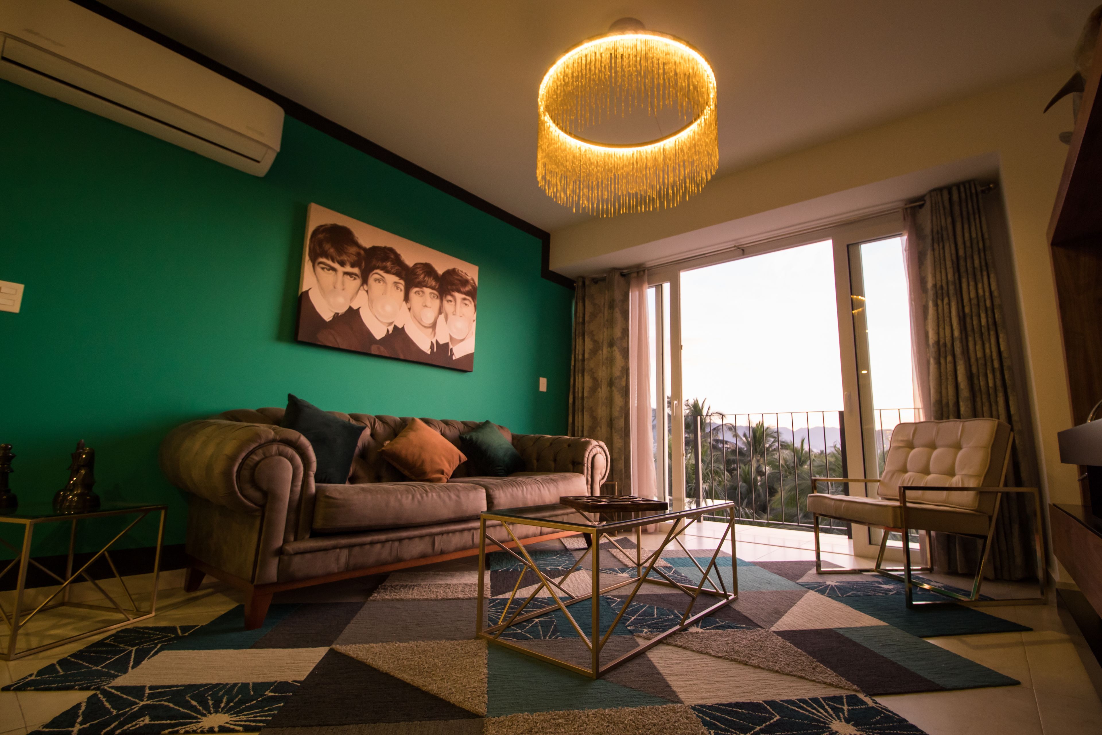 A living room with a green wall, a brown sofa, a patterned rug, a coffee table, and a chandelier.