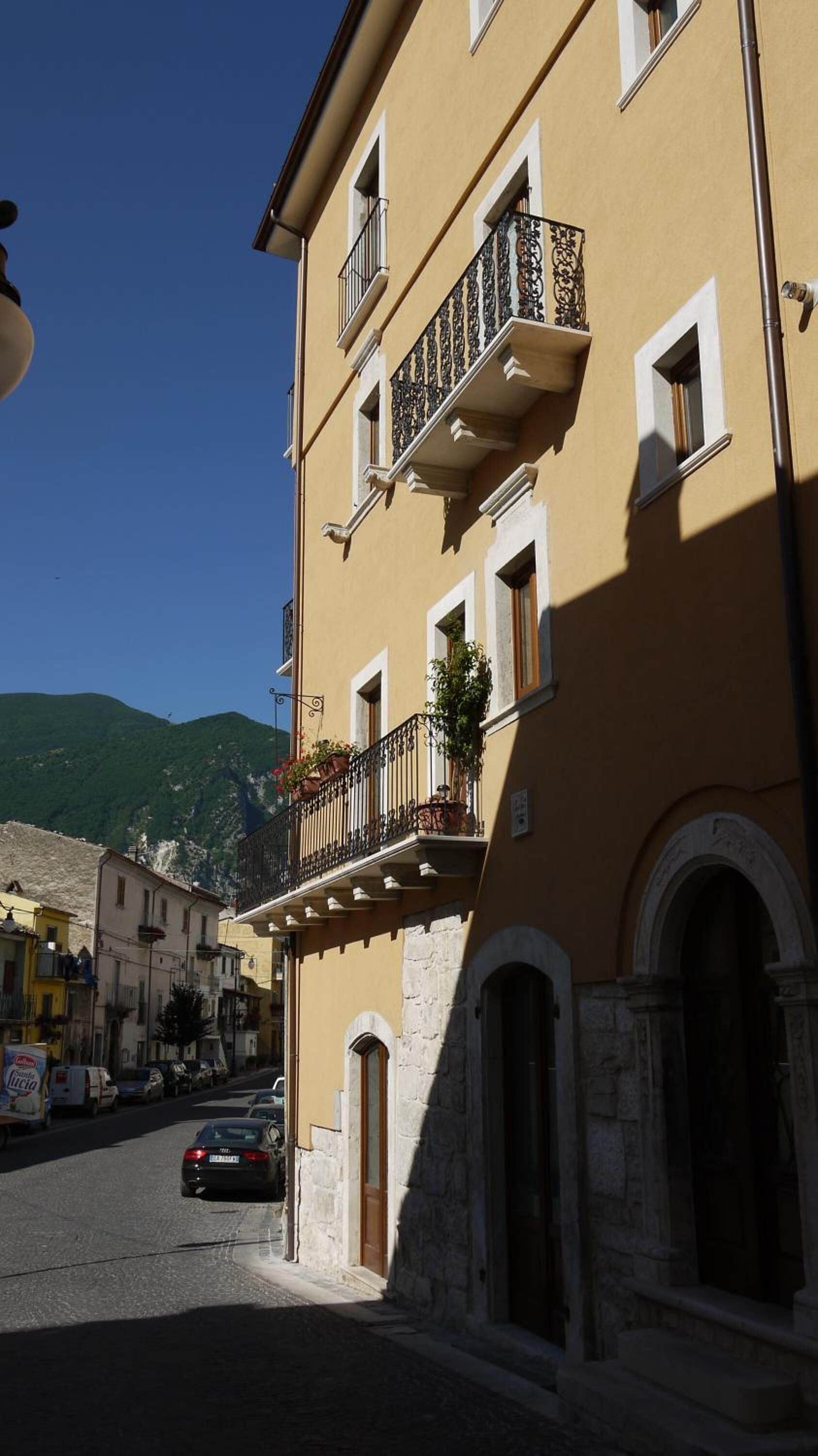A yellow building with a stone base, multiple windows, and a balcony with potted plants.