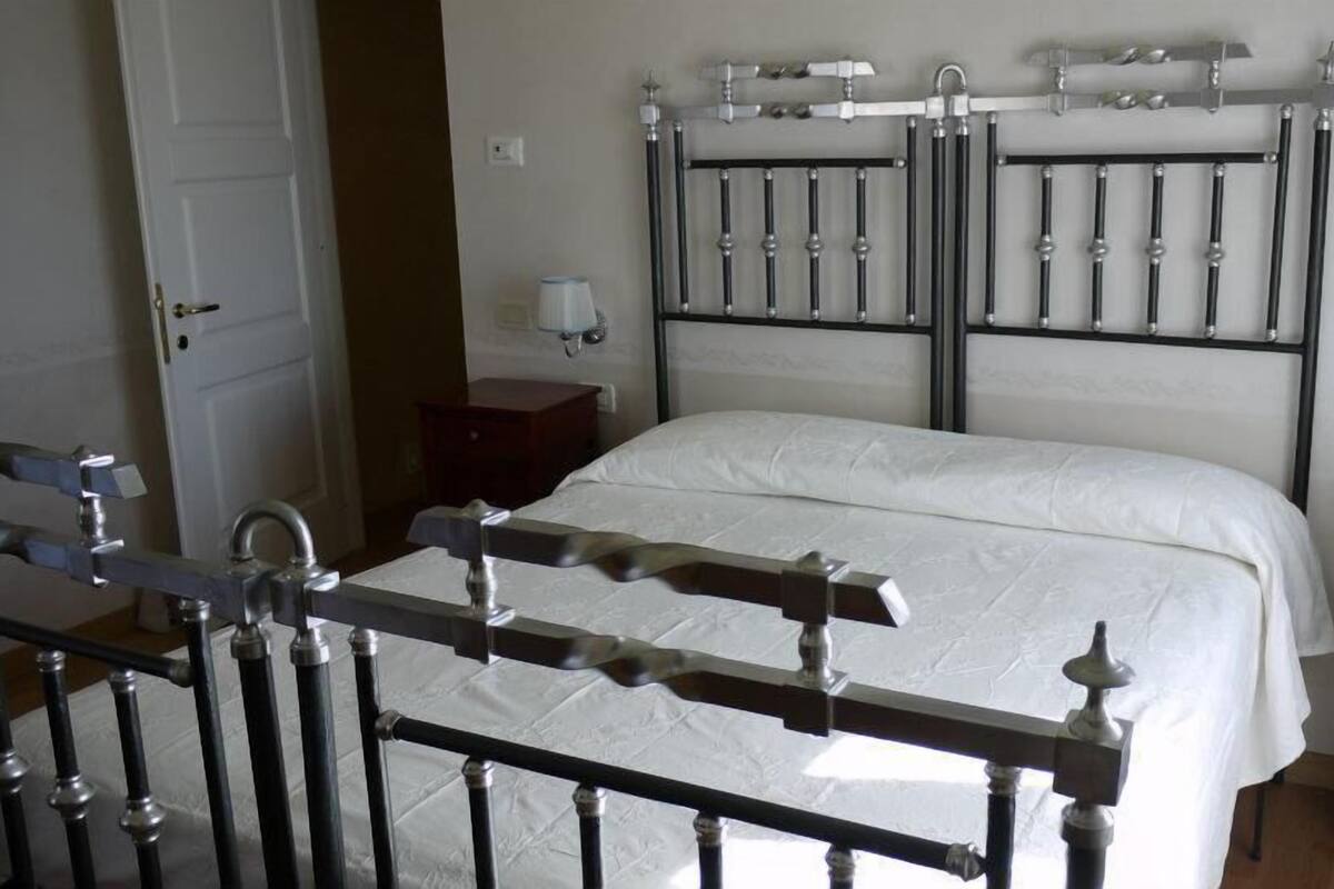 A bedroom with a bed, a nightstand, a dresser, a radiator, and a door.