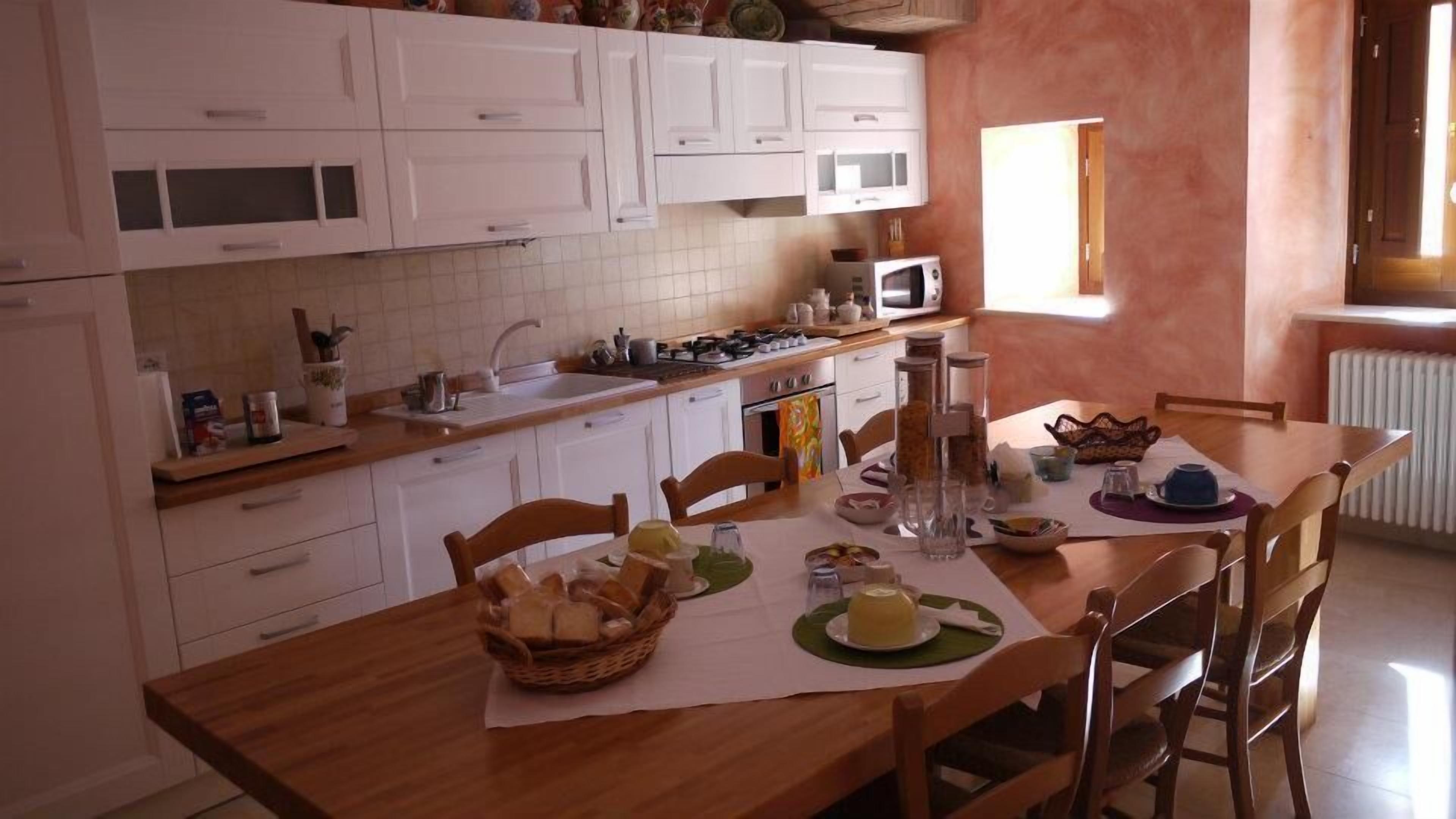 Een keuken met witte kastjes, een houten aanrecht en een eettafel gedekt met borden, glazen en een mandje brood.