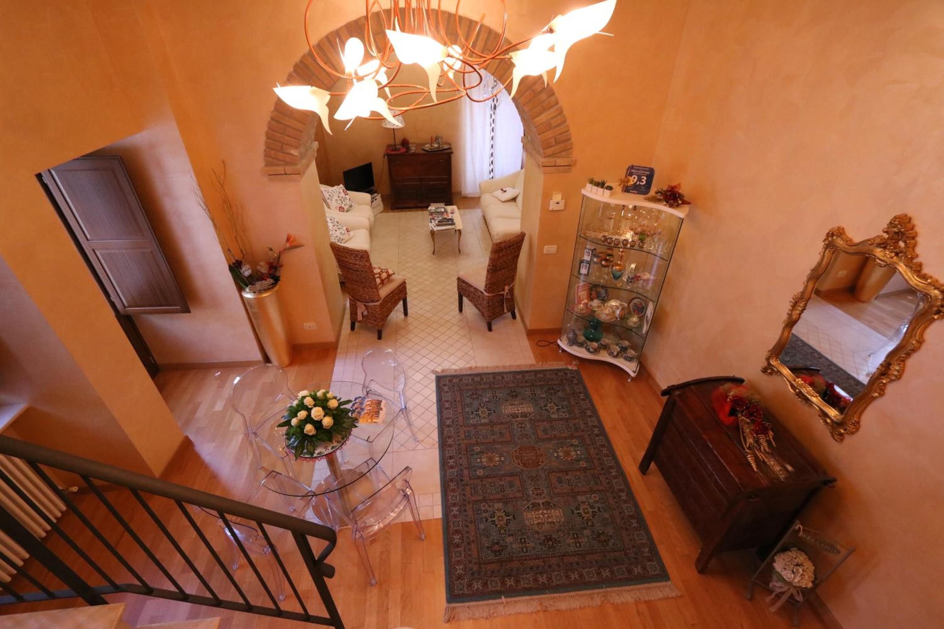 Amplia sala de estar con techo alto, candelabro, mesa de comedor con sillas, sofá, mesa de centro, alfombra, aparador con objetos decorativos y espejo en la pared.