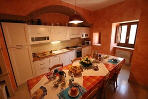 A kitchen with white cabinets, a microwave, and a dining table set with a checkered tablecloth. - B&B La Casa di Tocco (Tocco da Casauria)