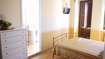 Una camera da letto con un letto, una cassettiera, una TV montata a parete e una porta che dà su un'altra stanza.