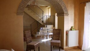 Un rincón acogedor con una escalera, sillas de mimbre, una mesita y un radiador.