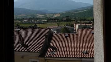 A view of a mountain range from a window overlooking a town with terracotta-tiled roofs and traditional buildings.
