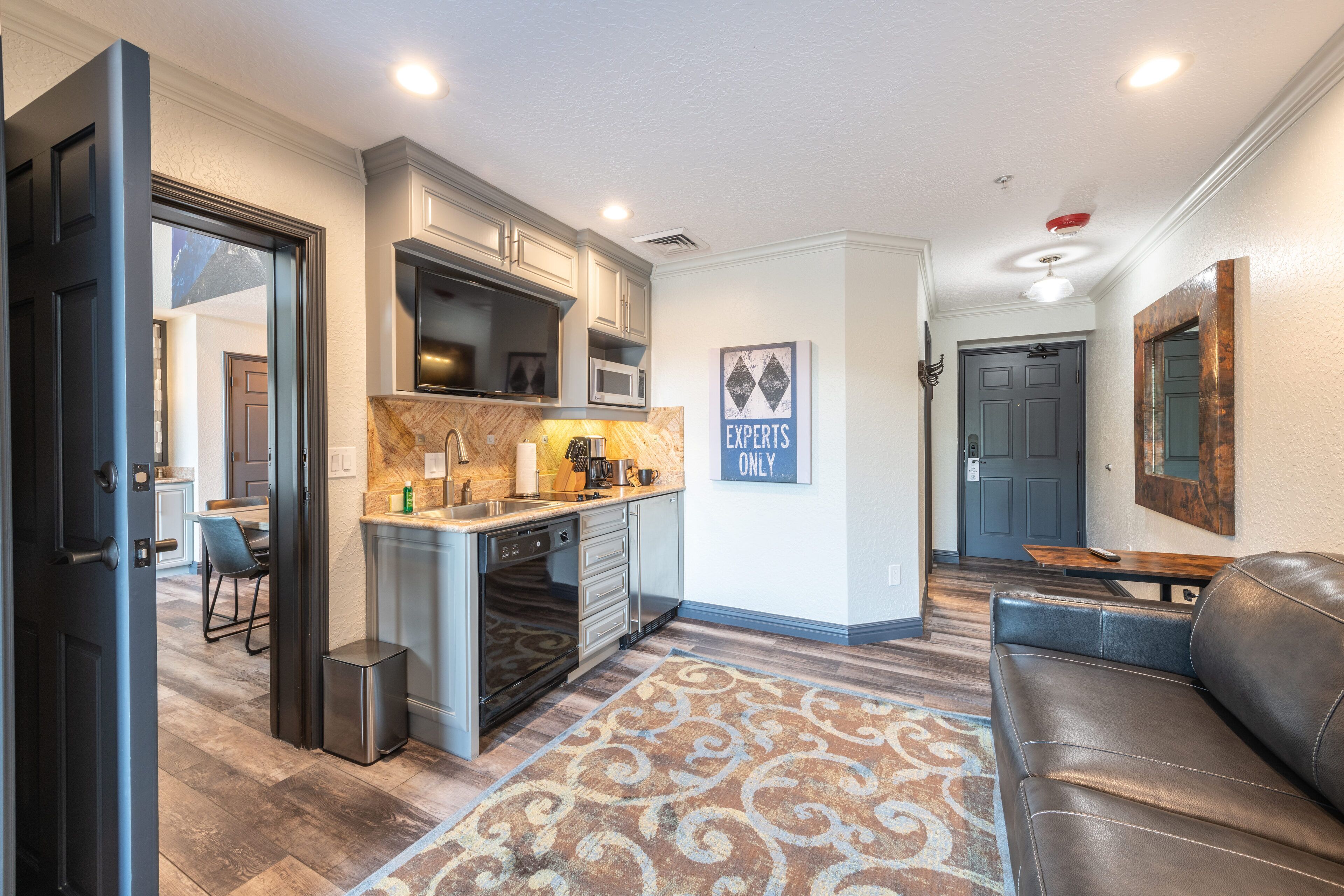 A modern kitchen with built-in appliances, a dining area with a table and chairs, and a leather sofa in a living room area.