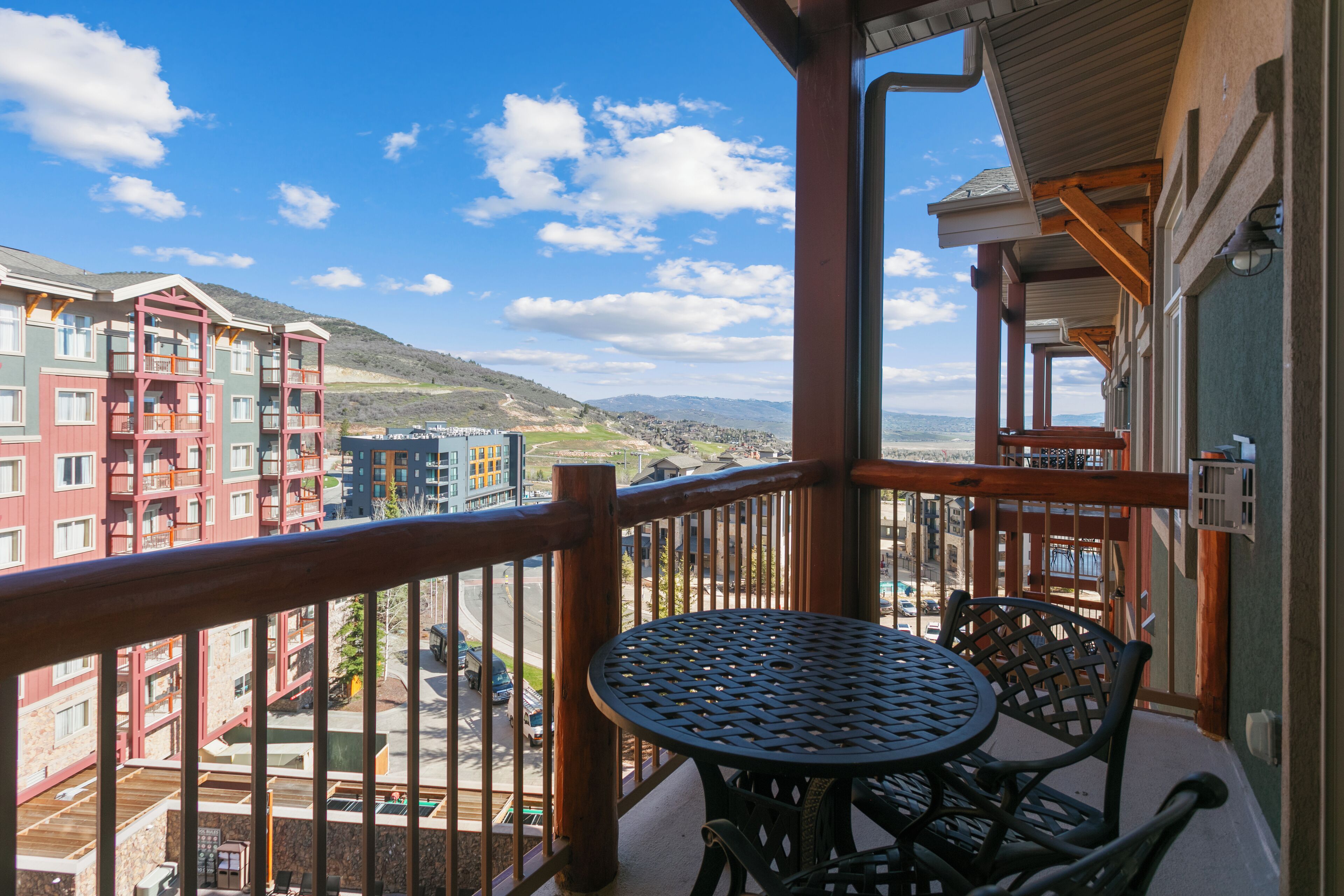 A balcony with a round table and chairs, overlooking a cityscape with buildings and a distant mountain.