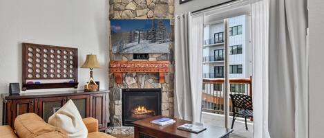 Una sala de estar con chimenea de piedra, un sofá, una mesa de centro y vistas a un balcón con barandilla.