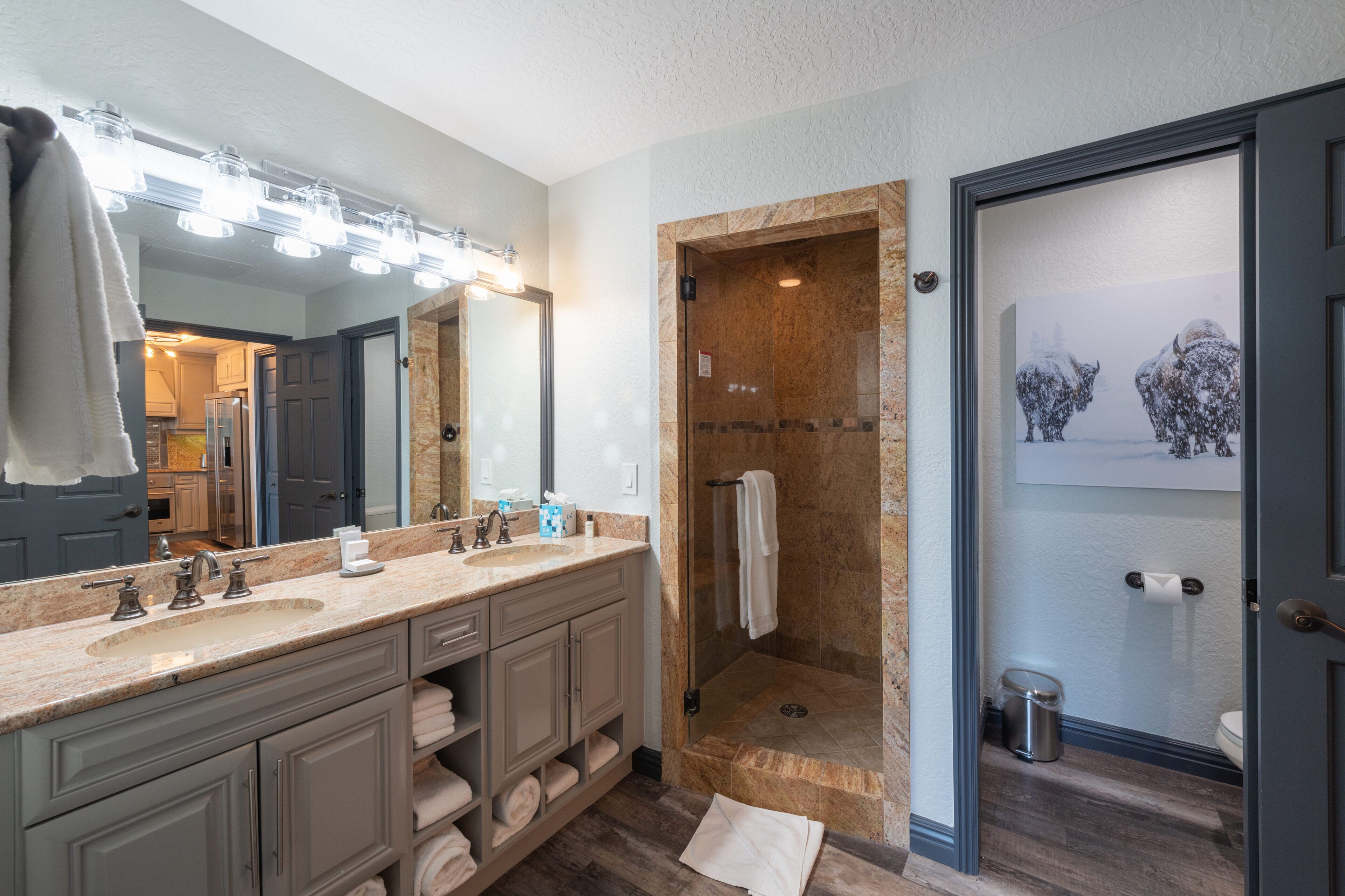 A bathroom with a large mirror, two sinks, a shower, and a toilet.