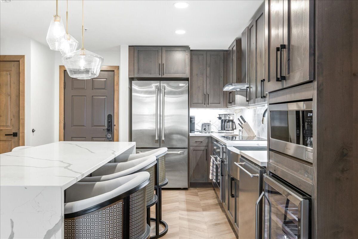 A modern kitchen with stainless steel appliances, a marble countertop, and a hanging light fixture.
