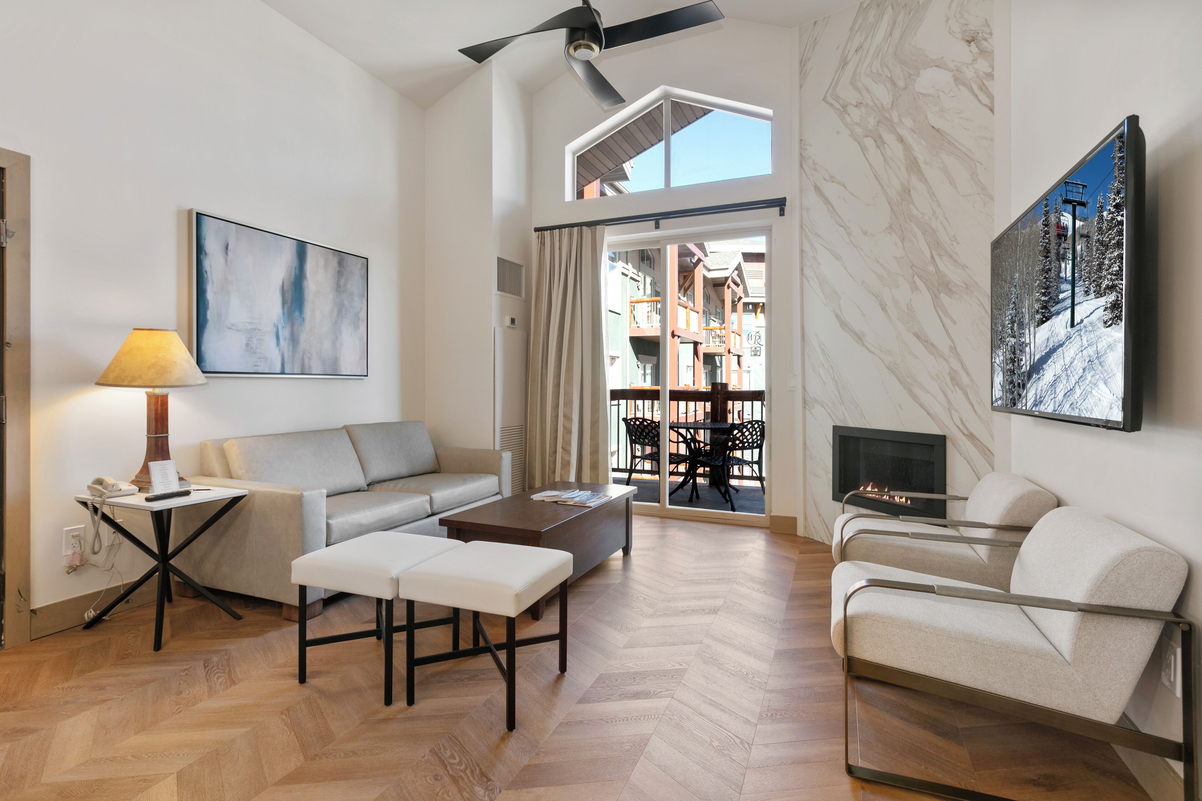 Una sala de estar moderna con sofá, mesa de centro y sillas, chimenea y balcón con vistas a edificios.