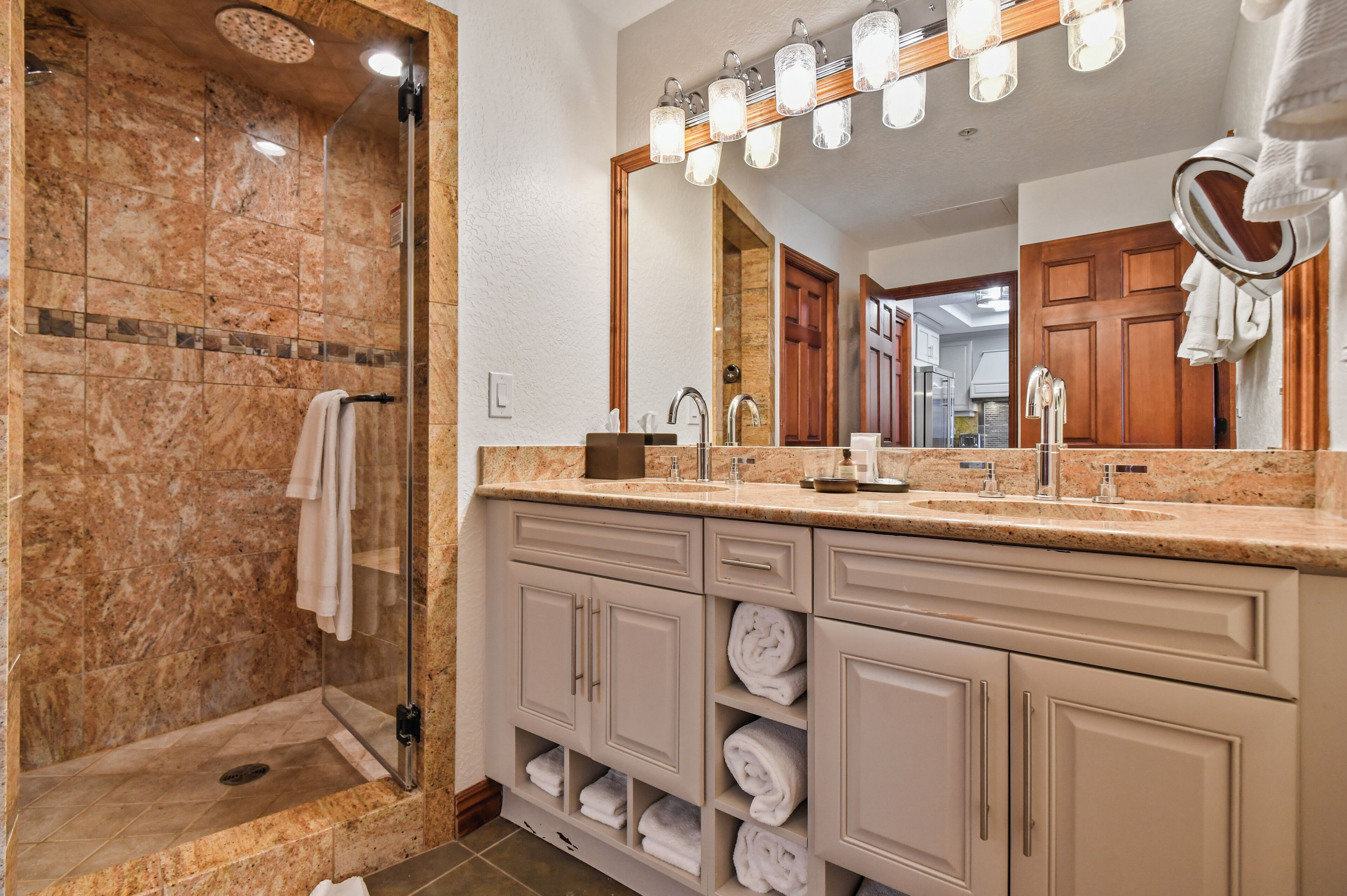 A bathroom with a glass-enclosed shower, a vanity with a large mirror, and neatly folded towels.