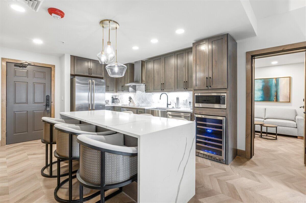A modern kitchen with a central island, stainless steel appliances, and a herringbone wood floor.