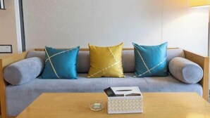 Un soggiorno moderno con un divano grigio, tre cuscini decorati e un tavolino in legno con un pacchetto di fazzoletti e un bicchiere.