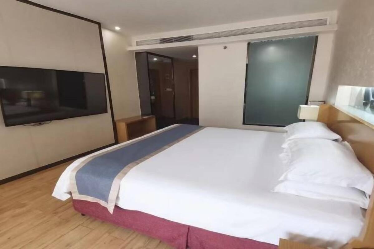 Habitación de hotel con una cama grande, un televisor de pantalla plana en la pared, un escritorio con una silla y una ventana con vidrio esmerilado.