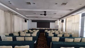 Una sala conferenze con file di sedie, un corridoio rivestito di moquette e un grande schermo nella parte anteriore.