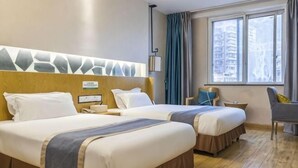 Una camera d'albergo con due letti, una testiera in legno, un tavolino, una sedia e una finestra con tende.