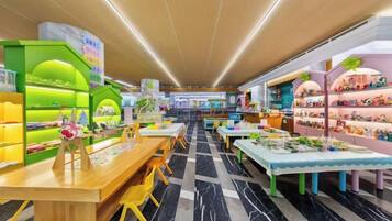 Un espacio interior luminoso con mesas, sillas, estanterías repletas de objetos y un suelo estampado.