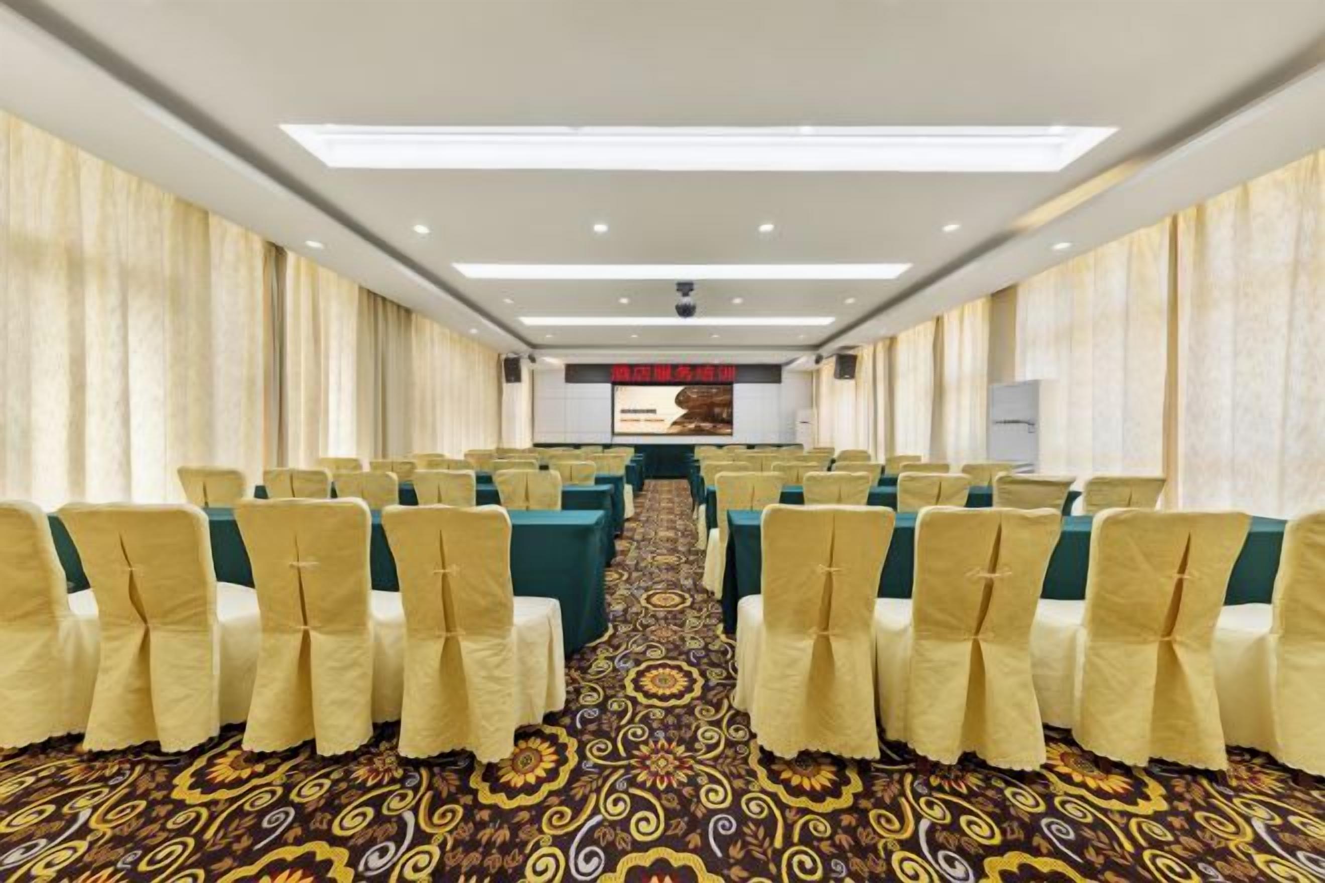 A conference room with rows of chairs, a carpeted floor, and a projection screen at the front.