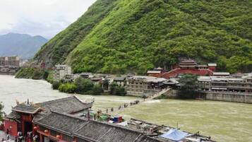 A traditional Chinese building with a steeply sloped roof, located beside a river with a bridge connecting to a hillside.