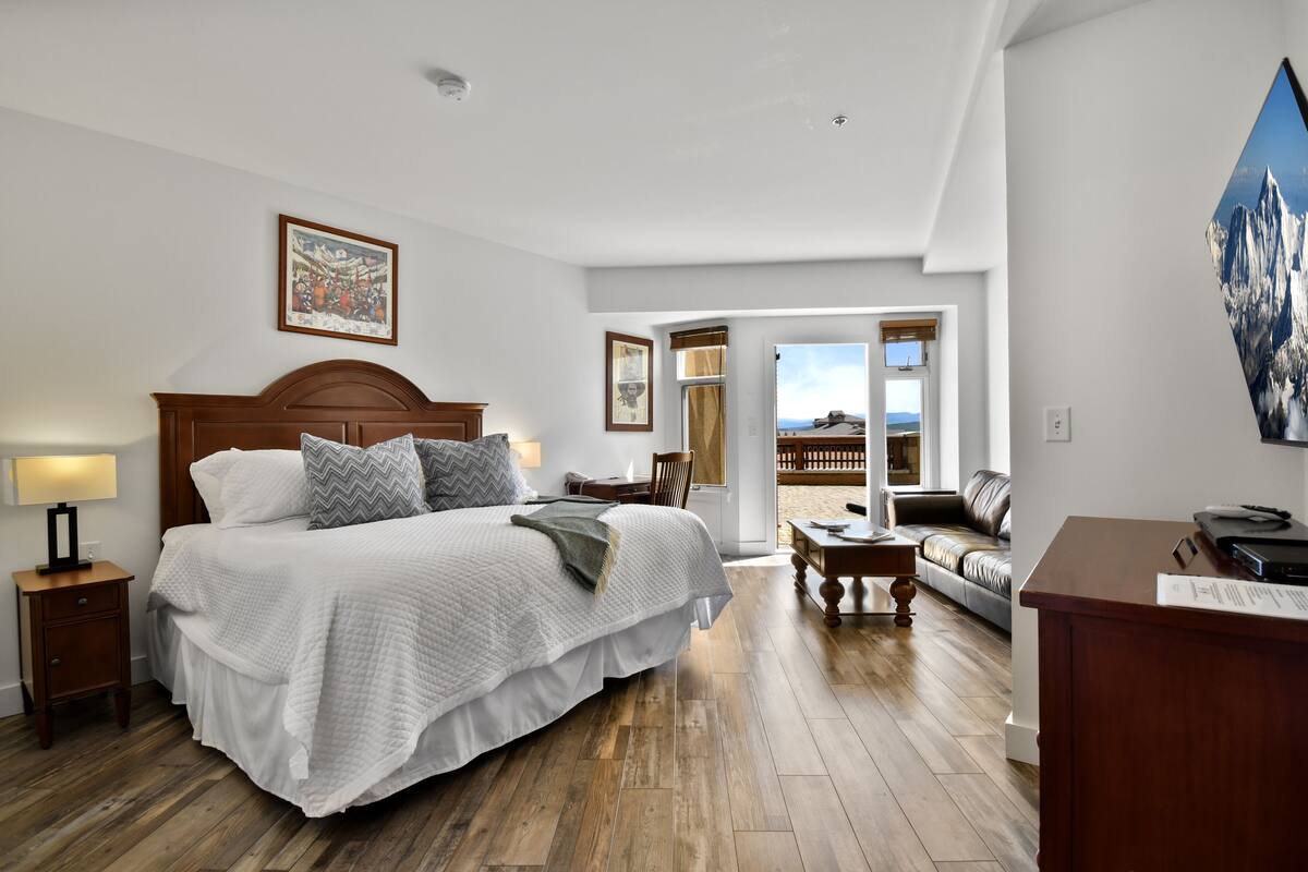 Ein Schlafzimmer mit einem großen Bett, einem Schreibtisch, einem Stuhl und Blick ins Freie.