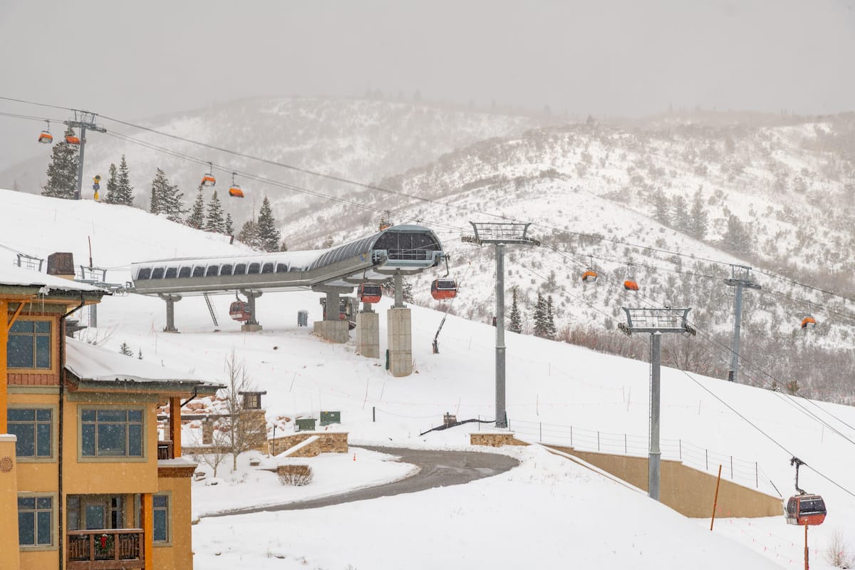 Eine Gondelbahn mit Sessellift, ein Gebäude mit Balkon und ein verschneiter Berggipfel im Hintergrund.