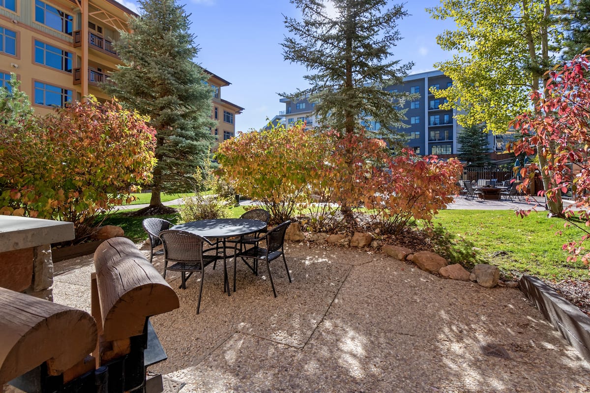 Eine Außenpatio-Terrasse mit Tisch und Stühlen, umgeben von Bäumen und einem Gebäude im Hintergrund.