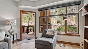 A modern living room with a grey armchair, a floor lamp, and a large window with a view of the outdoors. - Sundial Lodge (Park City)
