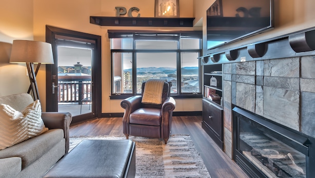 A living room with a fireplace, a leather armchair, a sofa, and a large window offering a view of the mountains. - Sundial Lodge (Park City)