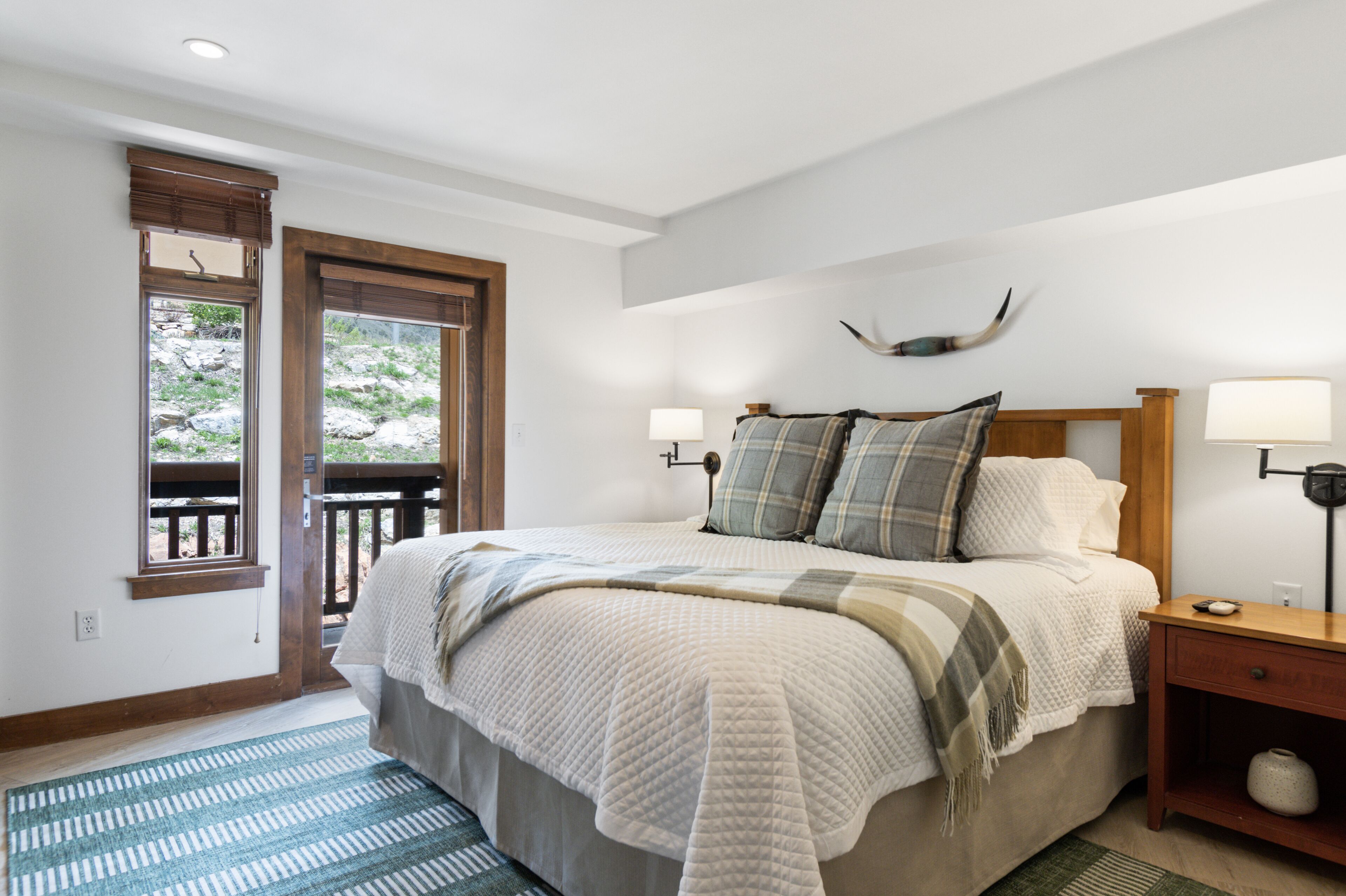 Une chambre à coucher avec un grand lit, deux lampes de chevet, une table de nuit en bois et une fenêtre donnant sur l’extérieur.