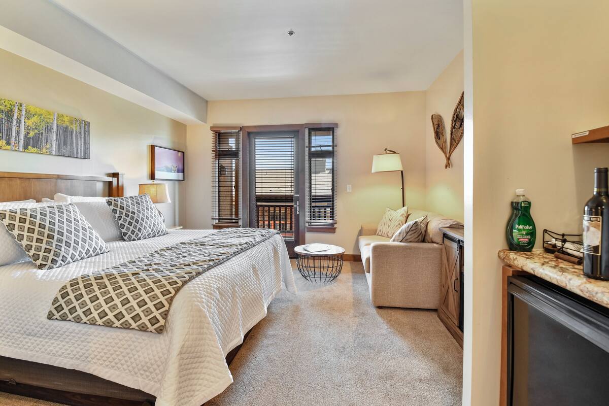 Ein Hotelzimmer mit Bett, Sofa, kleinem Tisch und Balkon mit Schiebetüren.