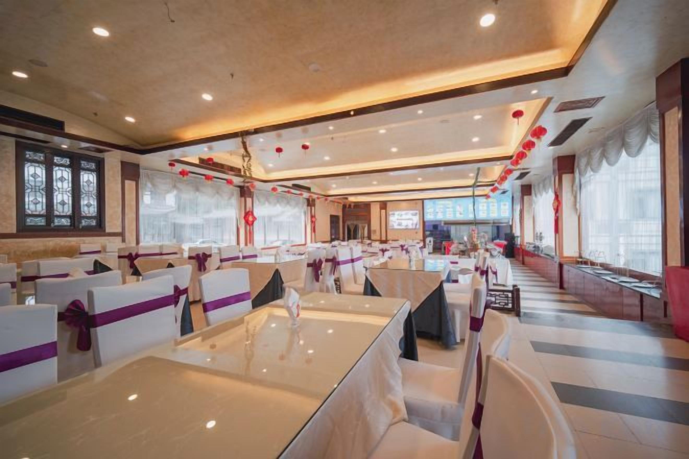Un salón de banquetes con varias mesas y sillas, amplias ventanas y un diseño de techo moderno.
