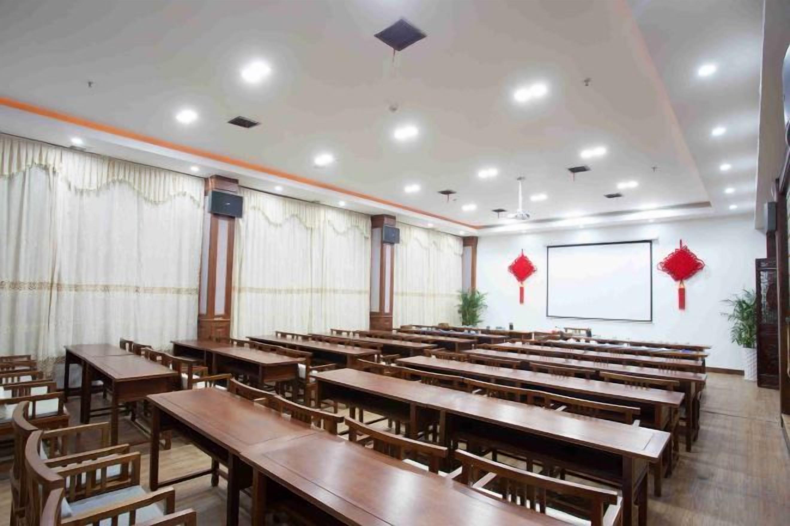 A conference room with multiple wooden tables and chairs, a large screen, and red decorations on the walls.