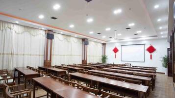 A conference room with multiple wooden tables and chairs, a large screen, and red decorations on the walls.