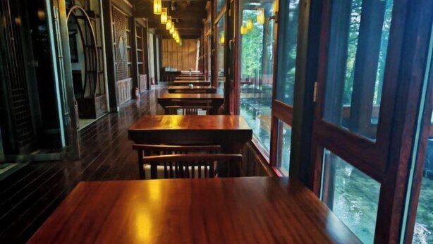 A row of wooden tables and benches in a restaurant with large windows. - Chabofu Charenju Hotel (Wuyuan)
