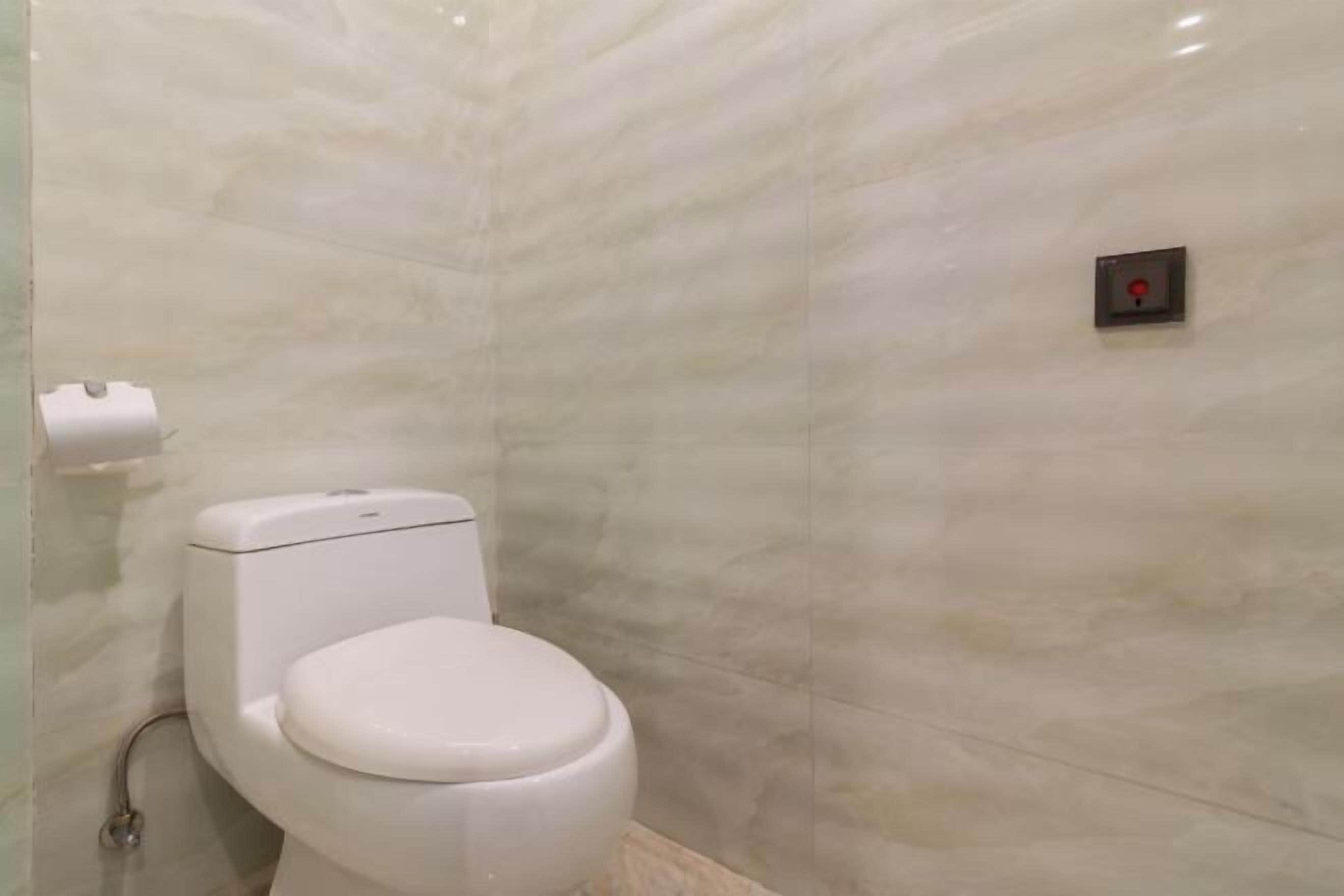 Een badkamer met een wit toilet, marmeren wanden en een spoelknop aan de muur.