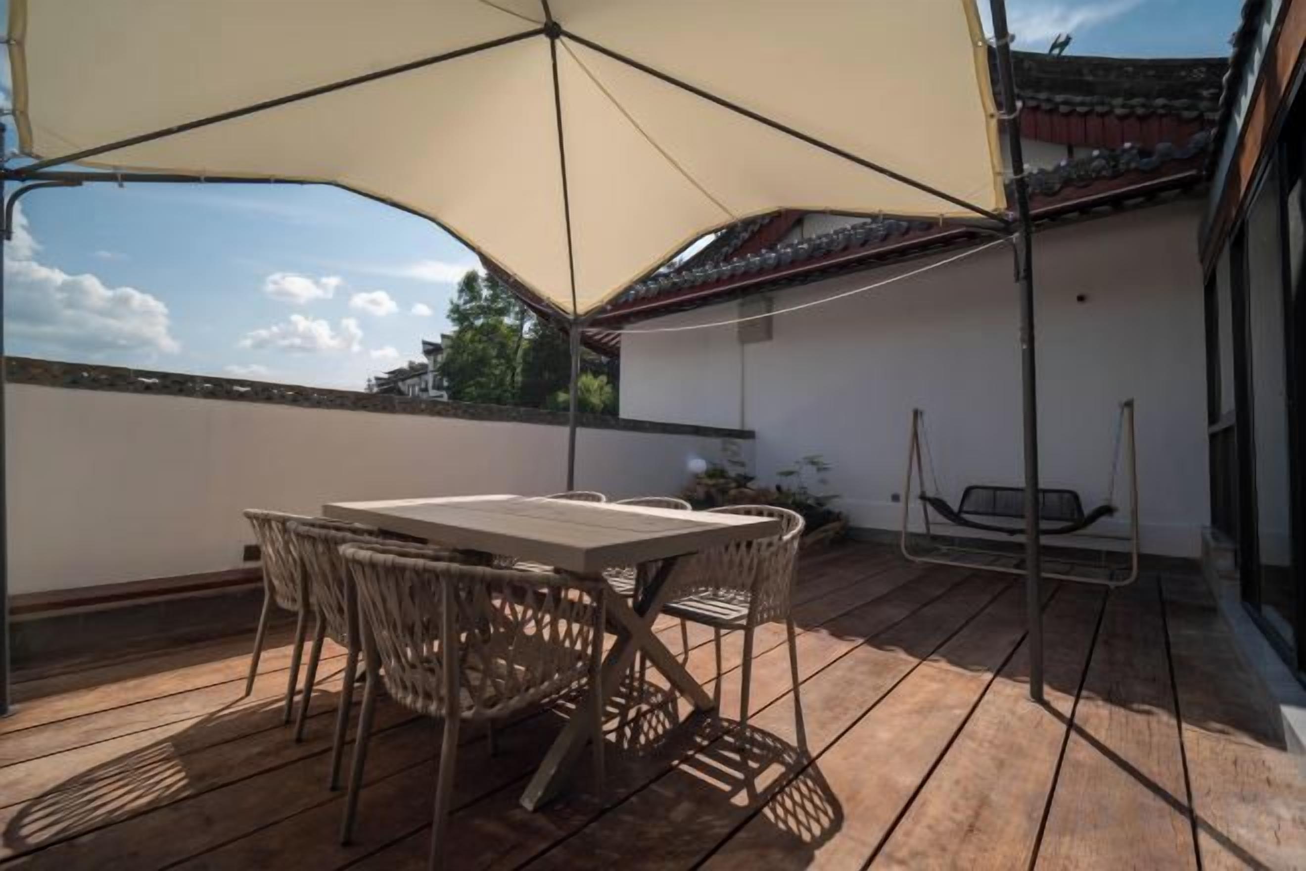 A covered outdoor patio with a table and chairs, a hanging swing, and a view of a traditional building.