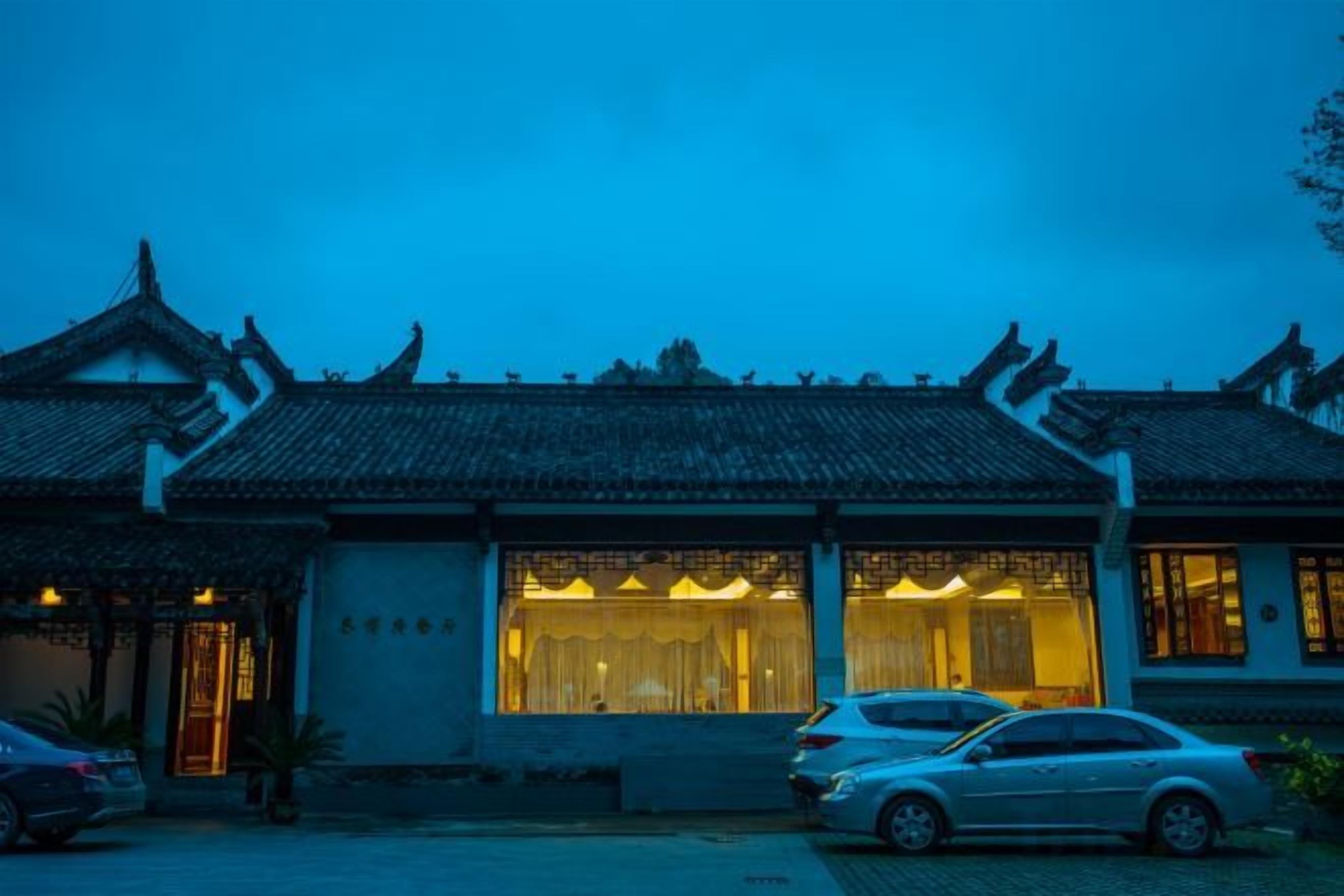 A traditional building with a tiled roof, a large window with curtains, and parked cars in front.