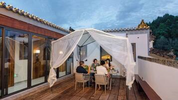 A covered outdoor seating area with a table and chairs, a glass enclosure, and a white canopy.