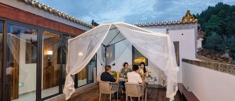 A covered outdoor seating area with a table and chairs, a glass enclosure, and a white canopy.