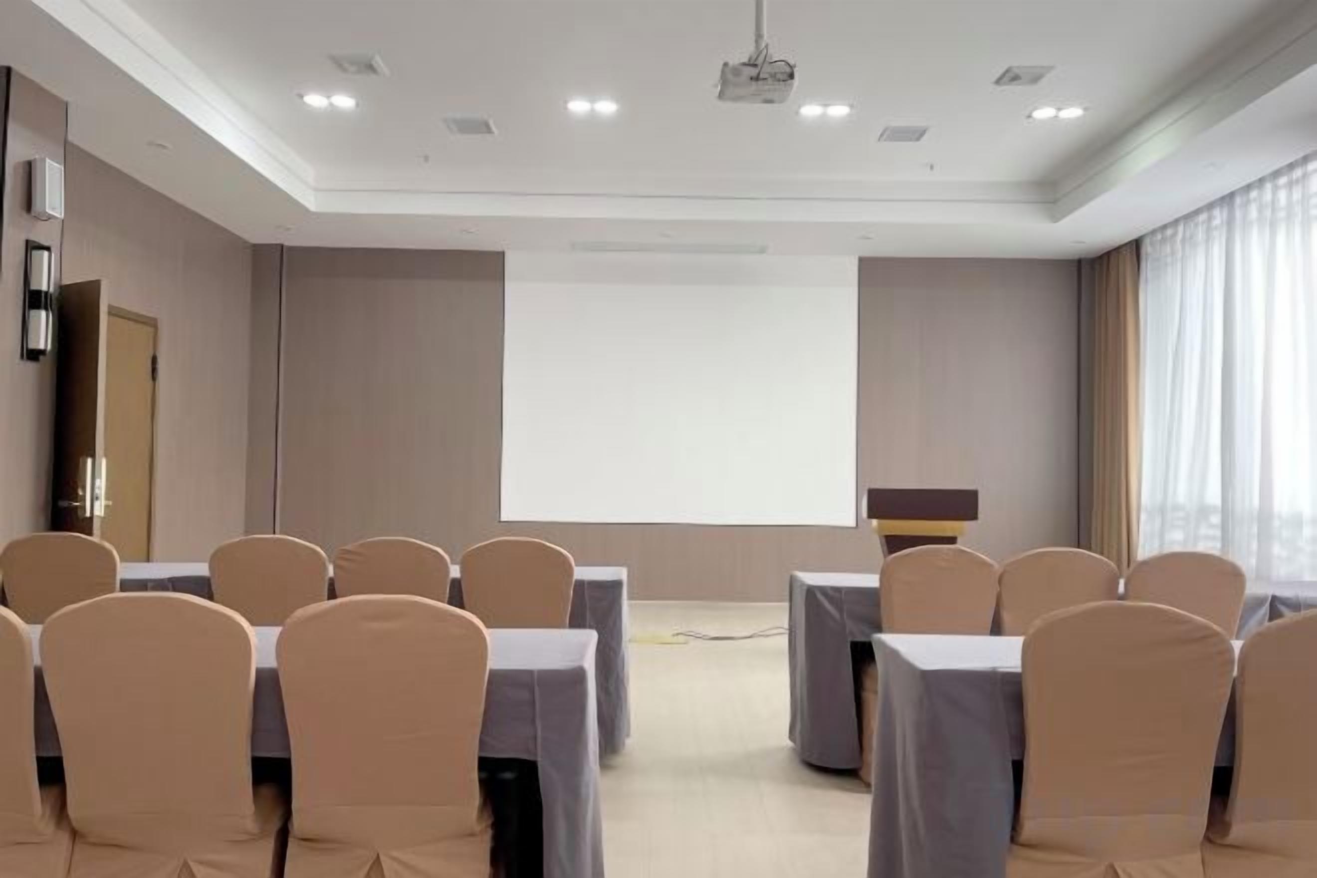 A conference room with a projector screen, tables, and chairs arranged for a meeting.