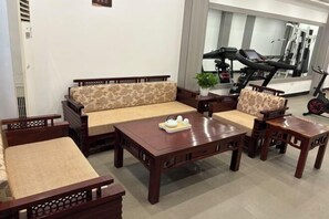 A living room with a sofa, two wooden tables, and a treadmill in the background. - Chabofu Charenju Hotel (Wuyuan)