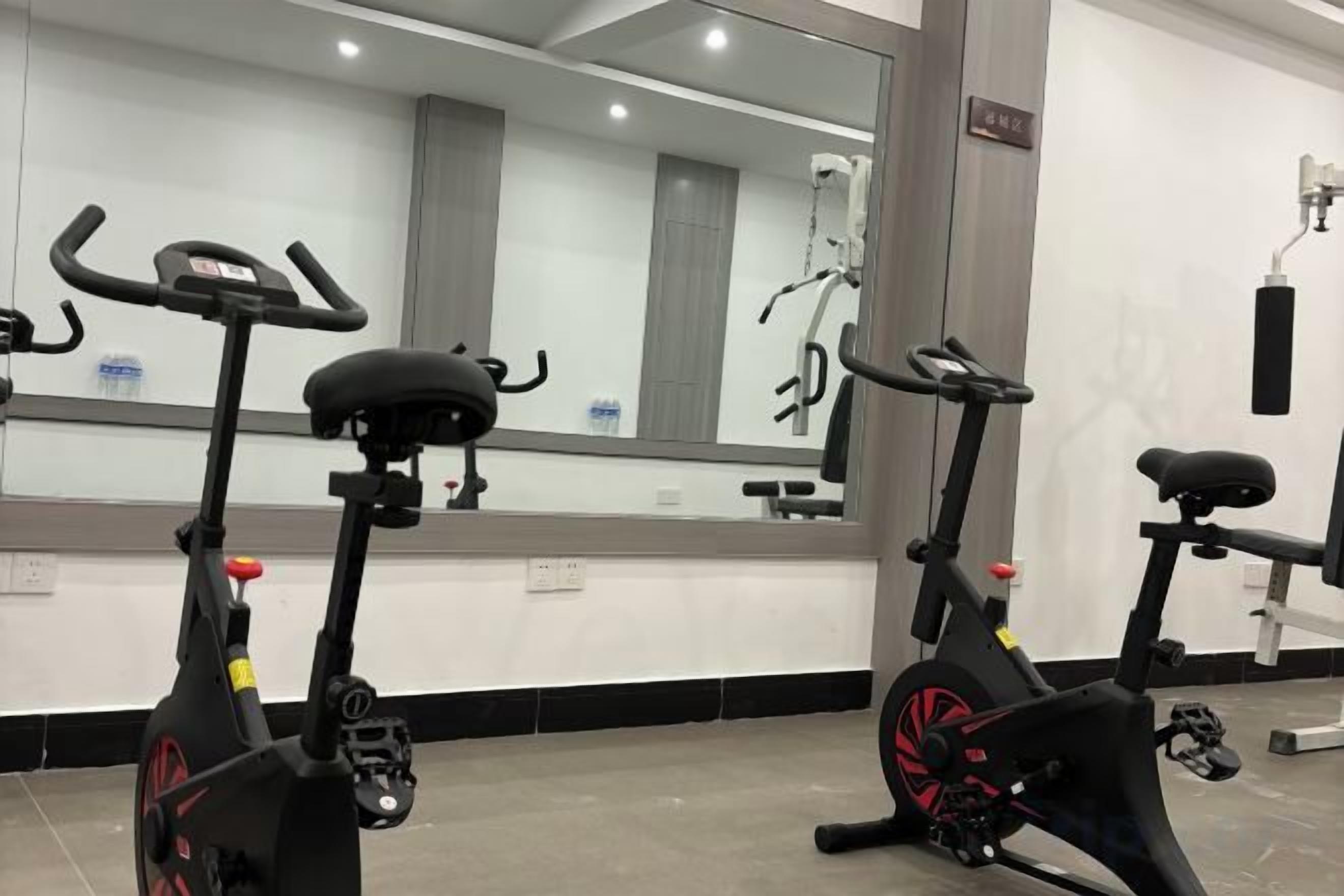 Twee stilstaande fietsen in een sportschool, met een grote spiegel en trainingsapparatuur.