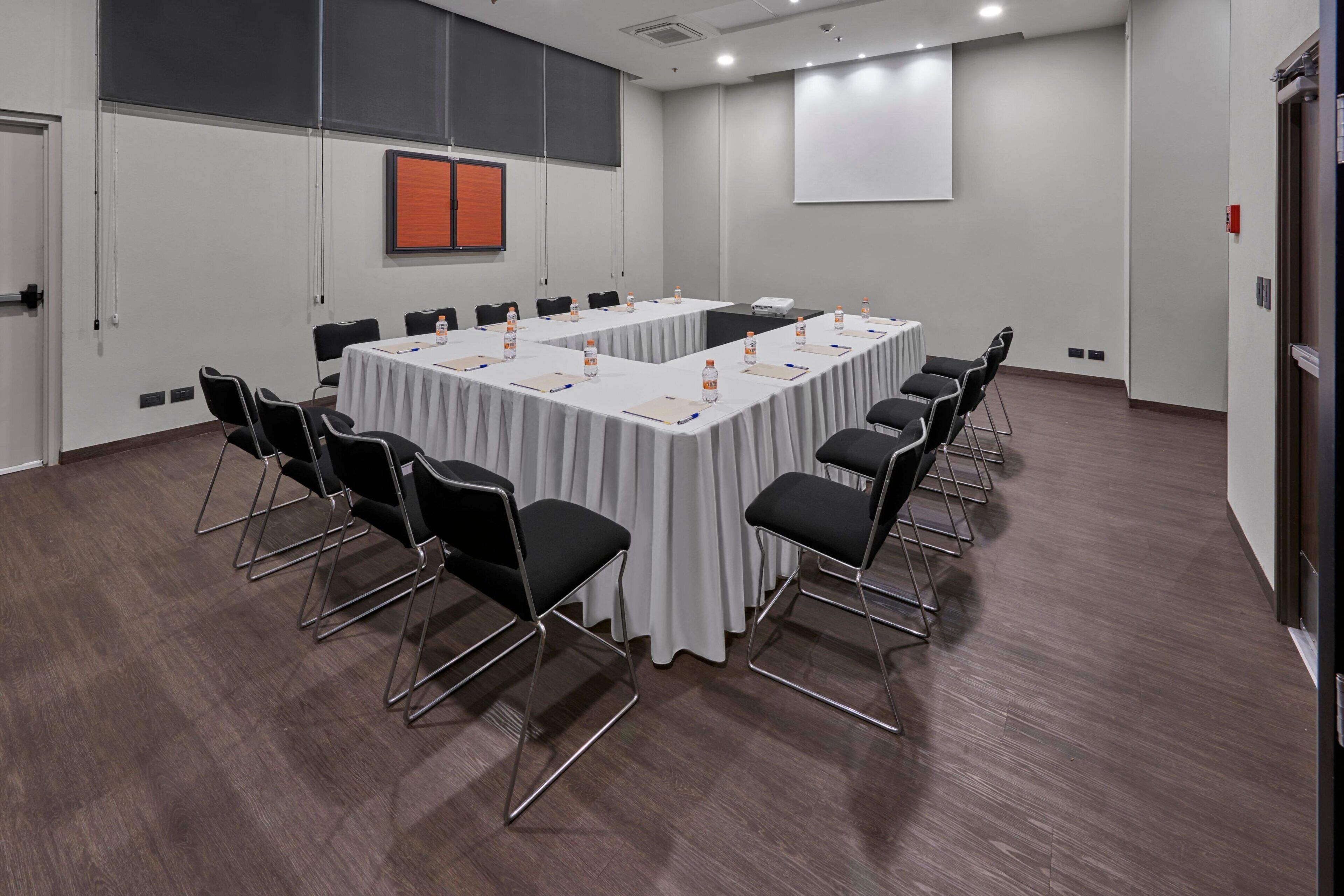 A conference room with a long table, chairs, a projector screen, and a whiteboard.